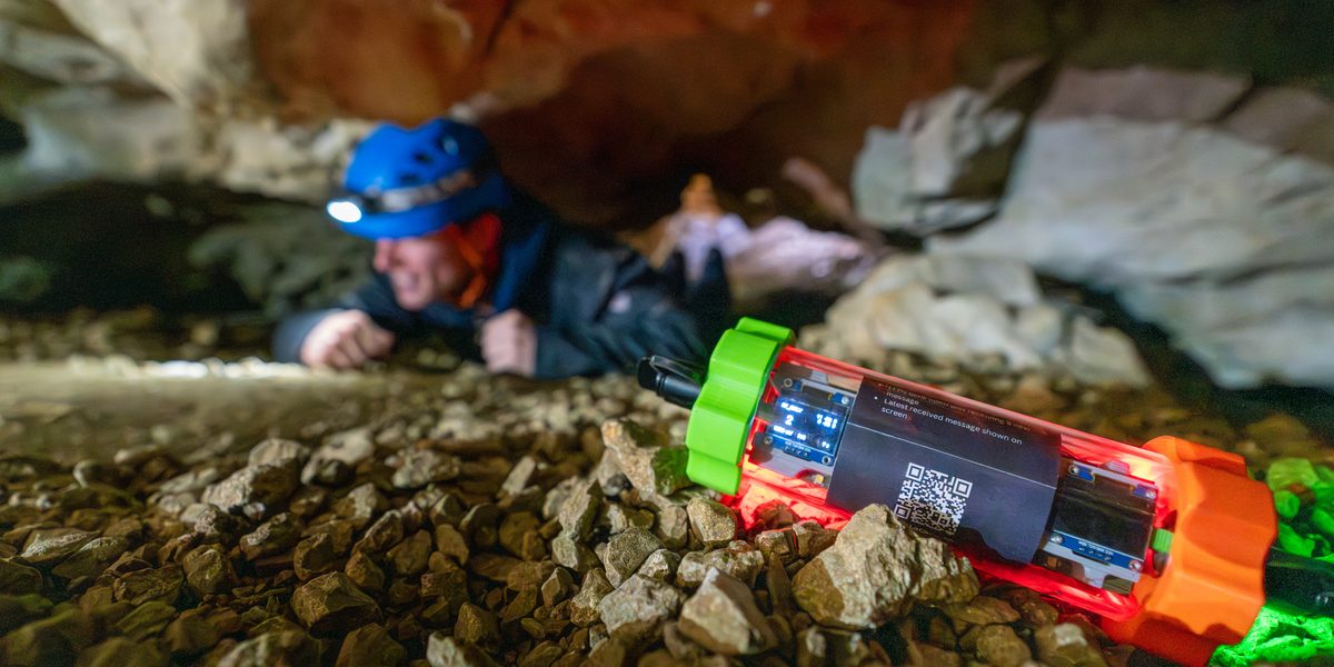 A LoCAVE endnode on the floor of a cave passage, with a caver crawling